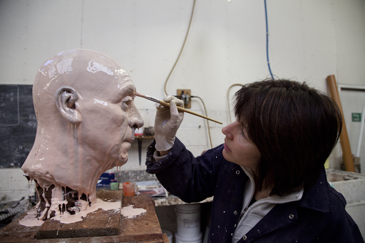 Craftsperson applying material with a brush to the surface of a large sculpted head