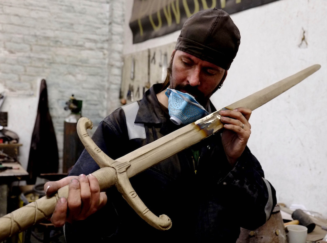 Craftsperson closely inspecting the surface of a long sculptural sword