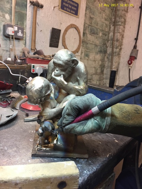 Gloved craftsperson working on an Affe mit Schädel bronze at the bench