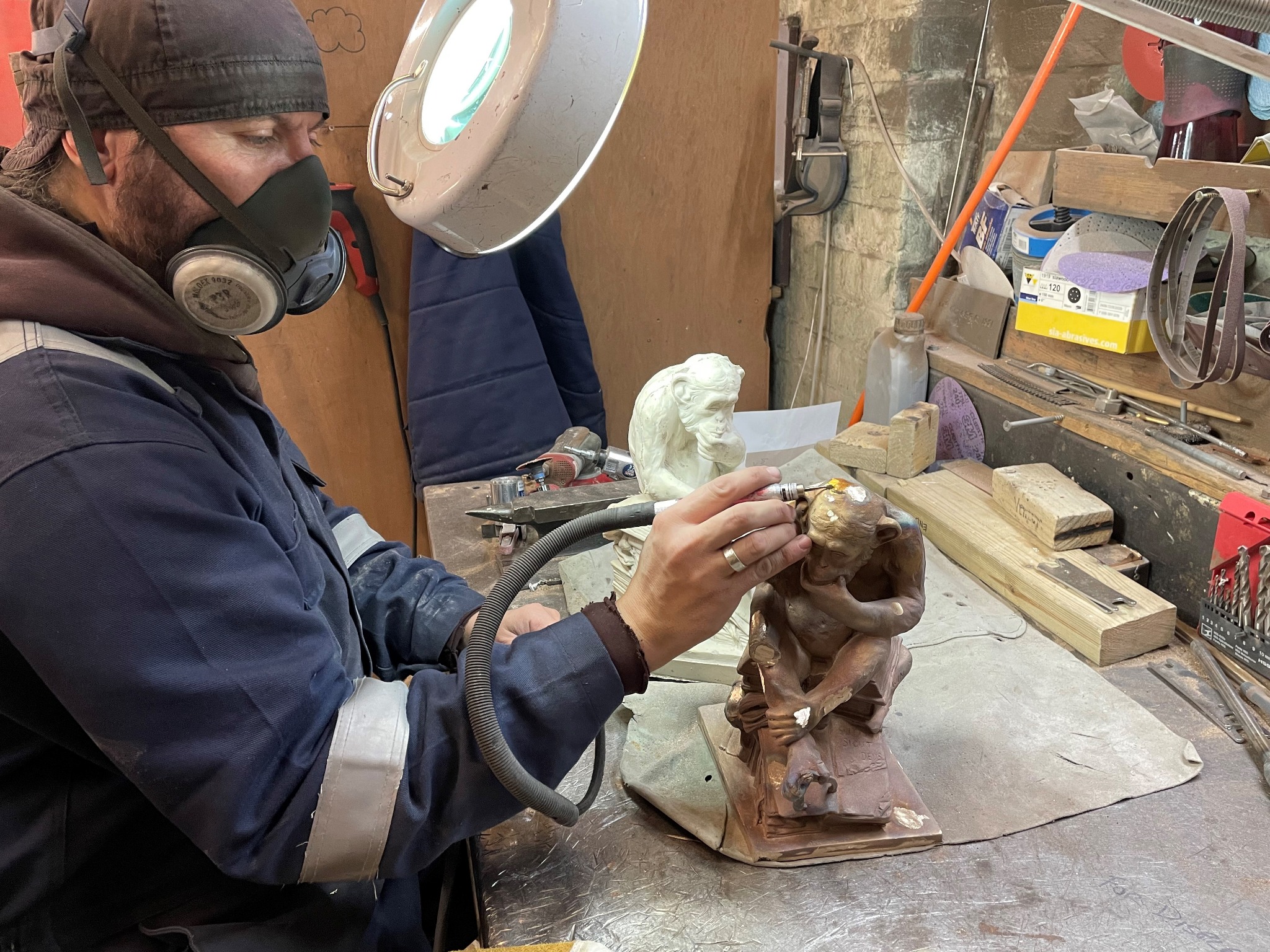 Foundry craftsperson wearing a respirator using a fine rotary tool on Affe mit Schädel